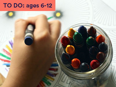 Close up of a hand holding a crayon next to a pot of crayons Keyword in the corner FOR FAMILIES