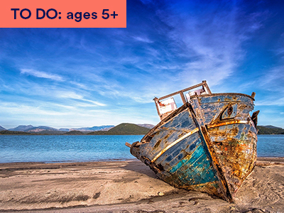 Photograph of washed up ship on sandy beach, blue sky and mountains. Keywords: TO DO: ages 5+