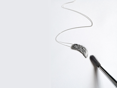 A paintbrush painting a piece of silver jewellery