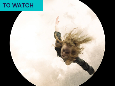 Heather Birleu wearing black dress is in spotlight in overhead shot. A white illuminated circle surrounds her as she dances. Keyword in the corner TO WATCH