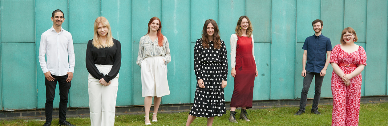 The seven 2020-21 Creative Pathways interns stand in front of the aqua background of the Lakeside Arts Pavilion building