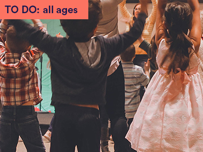 Photograph of children following instructor for a dance. Children with arms raised. Keywords: TO DO: all ages