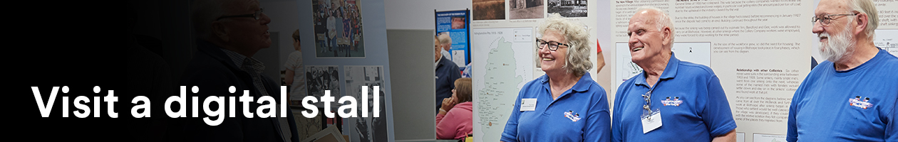 four people standing at a stall infront of banners with writing and images. Keywords: Visit a digital stall