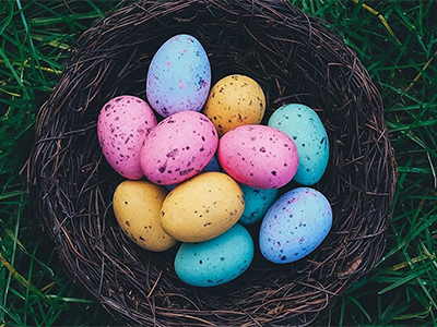 A photo displaying a basket full of pink, orange and blue Easter eggs