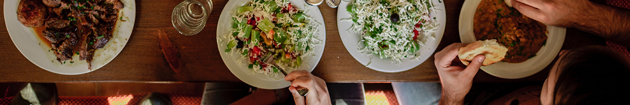 Food on table with many plates and people sitting and eating