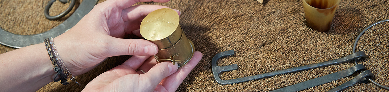 Photograph of hand holding a gold cup with other museum objects around