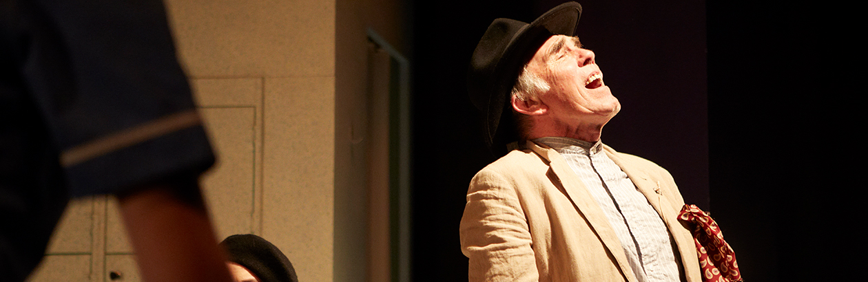 Photograph of Maurice Roëves on stage singing wearing a black hat and pale jacket 