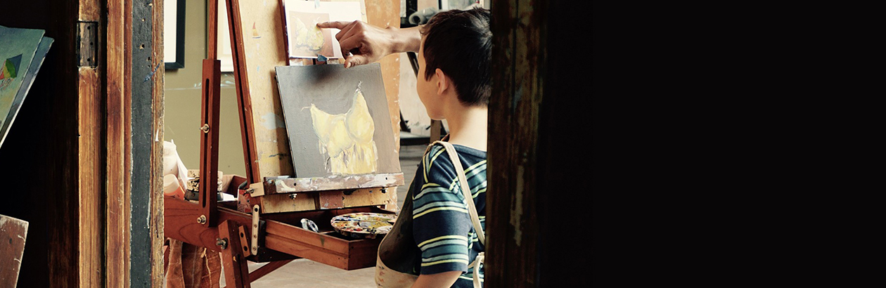 Photograph of a boy in a classroom in front of a painting easel learning