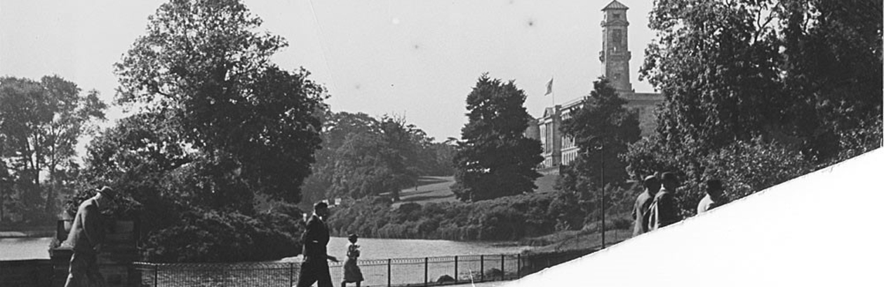 A black and white photo of people walking around Highfields Park, with the Trent building in the background