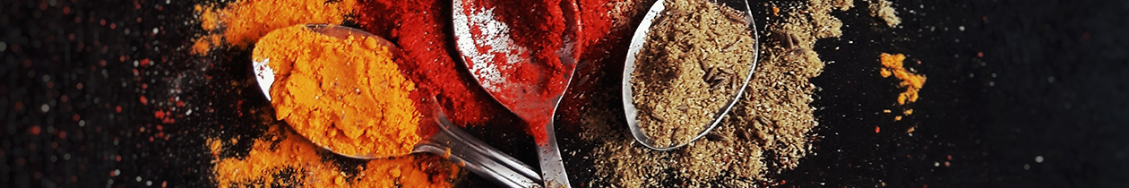 three spoons with orange, red and brown spices covering them on black background