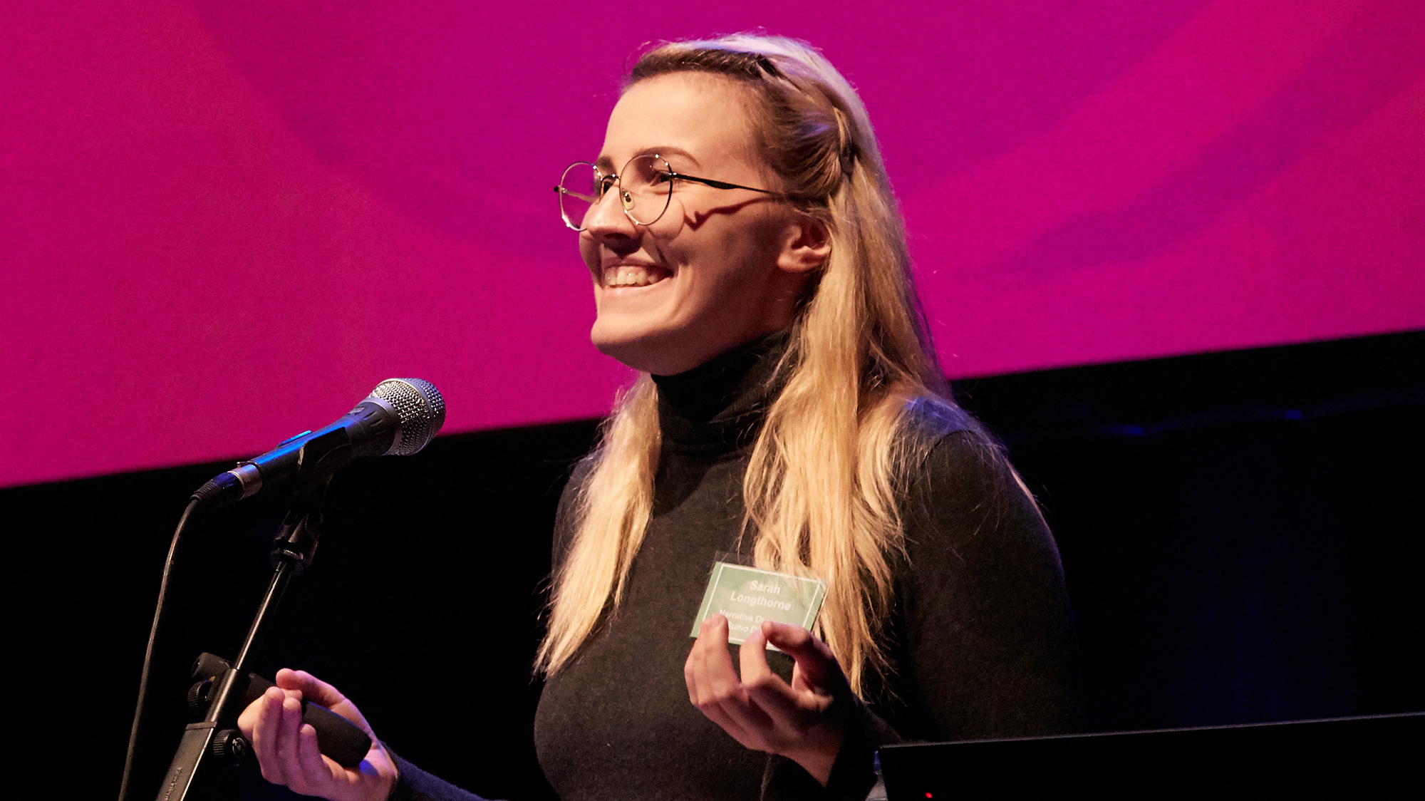 White woman standing in front of microphone wearing black top