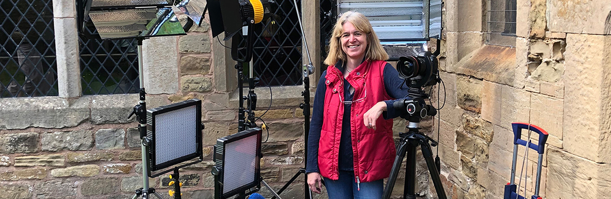 Photograph of Martine Hamilton Knight outside a building with camera around her