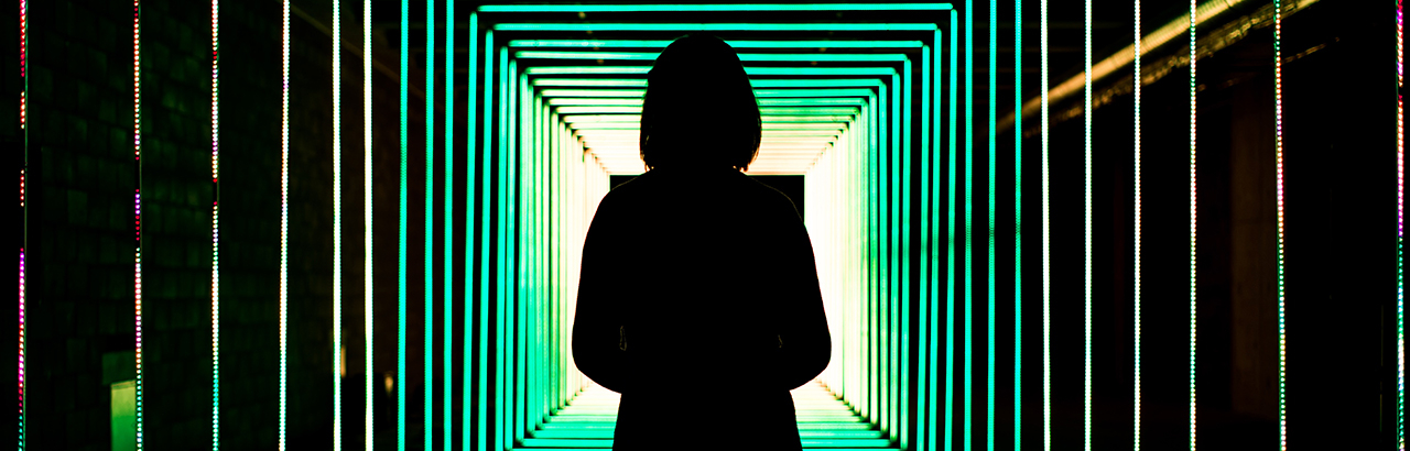 A silhouette of a girl looking down a tunnel lit by green lights