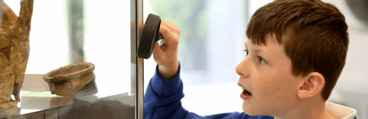 Boy in museum looking at object through a magnifying glass