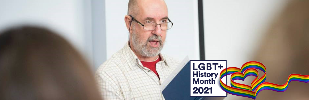 Professor Gregory Wood photographed holding a book. LGBT Rainbow banner with keywords: LGBT History Month 